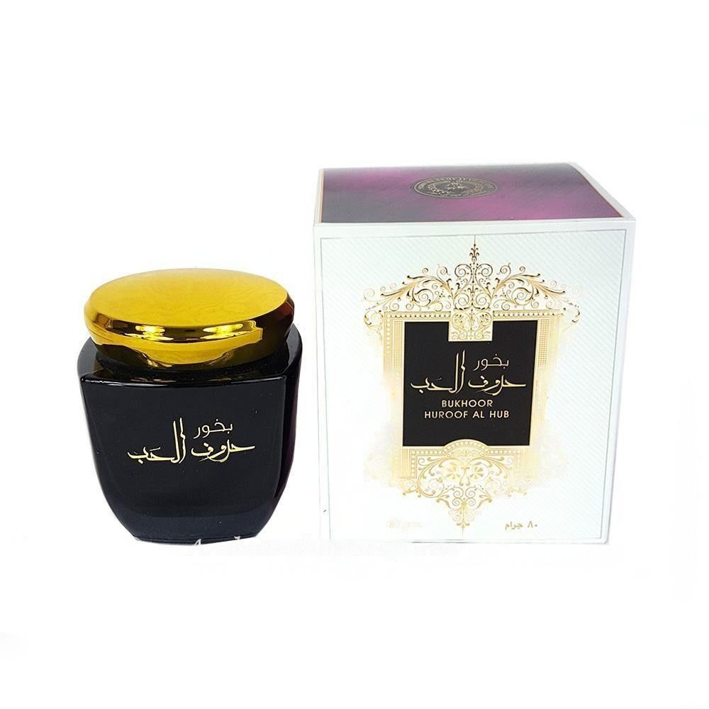 A black jar of Ard Al Zaafaran incense with a gold lid, next to a white box with gold and purple decorations, likely representing the product's packaging.