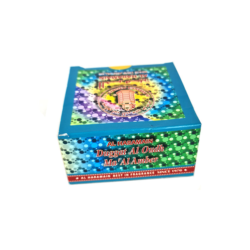 A colorful box of AL Haramain Duggat Al Oudh Ma'al Amber Bakhoor Incense with Arabic script on it.
