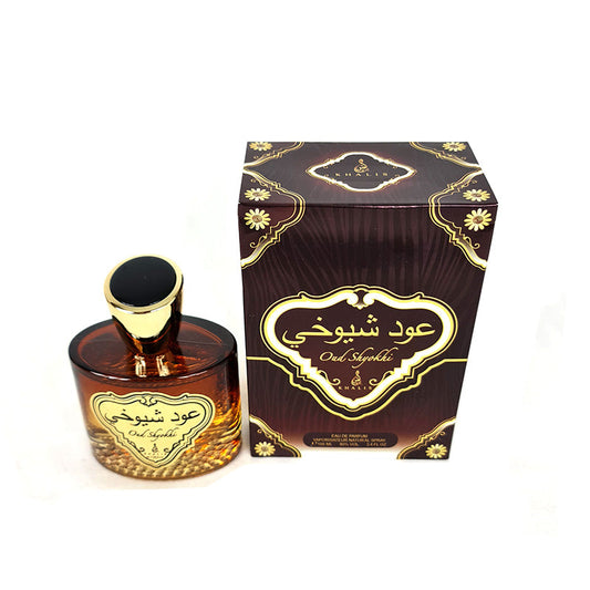 A bottle of Oud Shyokhi Spray Perfume by Khalis Perfumes alongside its packaged box. The bottle is brown with a gold-colored cap and the box has elaborate gold designs around the edges.