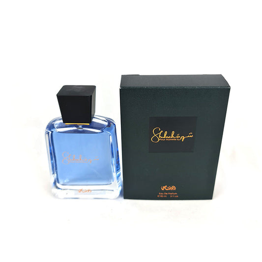 A SHUHRAH Men's 90ml EDP by Rasasi perfume bottle next to its black box with gold text.